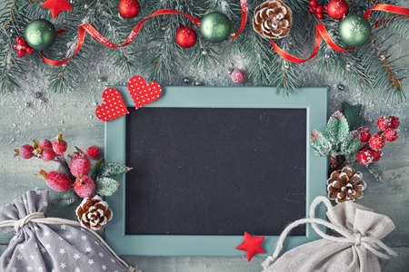 Decorated dark background with red and green decorations and fir twigs, text "Merry Christmas" on black-boardの写真素材