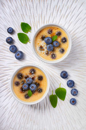 Creme brulee (cream brulee, burnt cream) with blueberry and lavender powdered with sugar on light wooden backgroundの写真素材