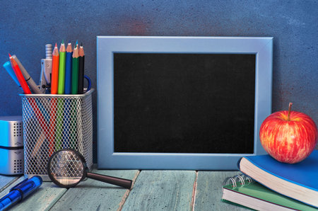 Stationery, apple and banana on a wooden table in front of blackboard with text space