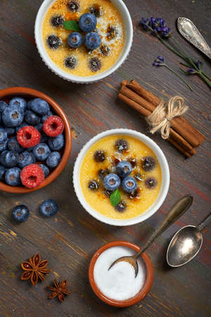 Creme brulee (cream brulee, burnt cream) with blueberry  powdered with sugar on dark rustic wooden backgroundの写真素材