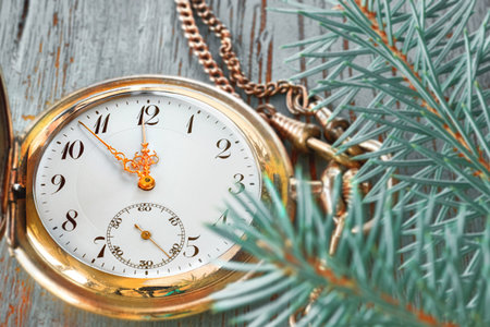 Vintage pocket watch showing five to twelve on gray rustic background with fir twigs and golden...