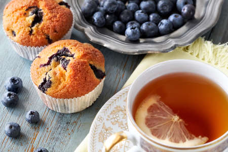 Close-up on blueberry muffin and cup of tea with lemon on gray rustic wooden tableの写真素材