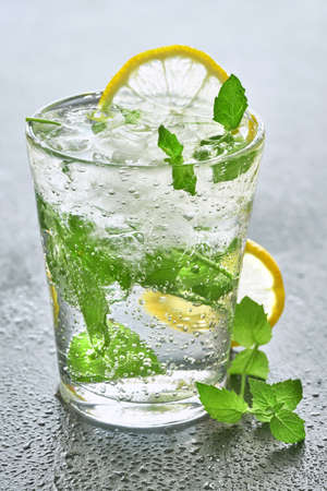 Close-up on a glass of sparkling water with lemon and mint on a grey stone backgroundの写真素材