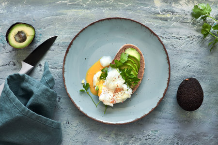Avocado sandwich with dark bread, sliced avocado and poached egg, flat lay on turquoise rustic