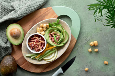 Keto diet, top view of avocado rose salad with bacon cubes and smoked cheese seasoned with lemon, mint leaf and sea salt on green texturedの写真素材