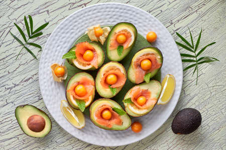 Avocado boats with smoked salmon, lemon, physalis and mint leaf, top view on light texturedの写真素材