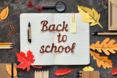 Back to school cut-out text, flat lay on dark texture  with stationary, Autumn leaves