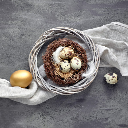 Easter flat lay on dark background with quail eggs in the nest, linen fabrique and two golden eggs....