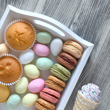 Easter flat lay with macarons, muffins and marzipan eggs jn a decorative tray on textured grey wood