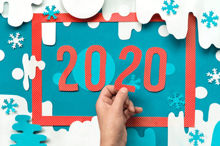 Happy New Year 2020! Paper craft, red frame on paper winter background with hand holding number 2,...