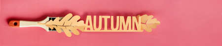 Flat lay on paper, paint brush with paper oak leaves and text "Autumn" on coral background, panoramic image for banner designの写真素材
