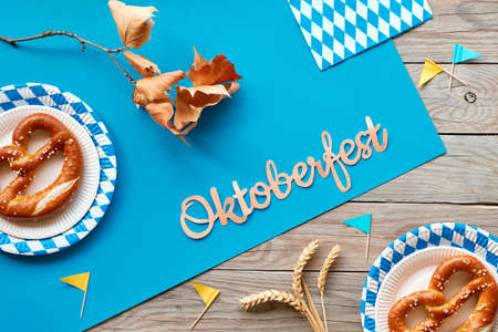 Oktoberfest, flat lay on rustic wooden table with blue paper spread, pretzels on disposable plates, wheat ears, decorative flags and Autumn leavesの写真素材