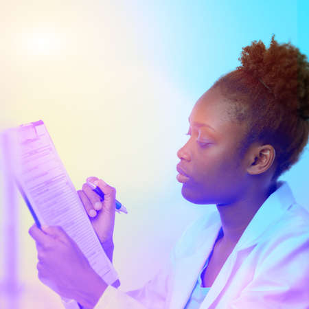 African scientist, medical or or graduate student. Confident young woman wearing lab coat holds a pen and a questionnaire. Square composition, futuristic neon glow, focus on the eyesの写真素材