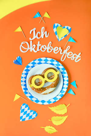 Paper text "I love Oktoberfest" in German, flat lay on orange paper background with pretzel on paper plate, decorative hearts, flags and Autumn leaves.の写真素材