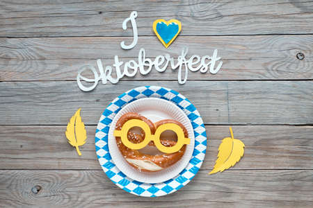 Paper text "I love Oktoberfest", flat lay on rustic wooden table with pretzels on paper plate, decorative hearts, flags and Autumn leaves.の写真素材