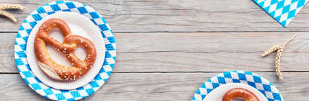 Oktoberfest rustic background. Two prezels in blue and white checkered disposable paper plates. Flat lay on rustic wooden table decorated with wheat ears, banner composition with copy-space.の写真素材