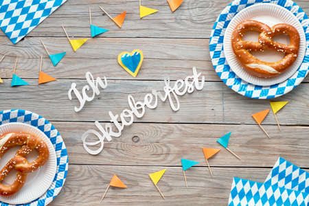Paper text "I love Oktoberfest" in German, flat lay on rustic wooden table with pretzels on paper plate, decorative hearts, flags and Autumn leaves.の写真素材