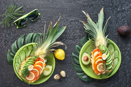 Top view on pineapple boats with smoked salmon and avocado slices with lemon and quail eggs, flat lay on dark textured backgroundの写真素材