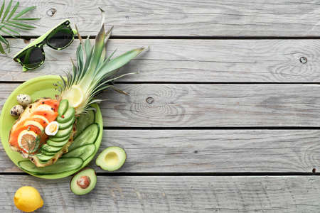 Top view on pineapple boats with smoked salmon and avocado slices with lemon and quail eggs, flat lay on old wooden tableの写真素材