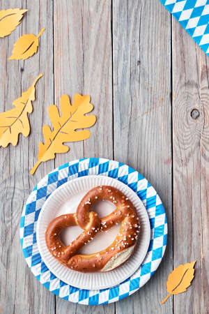 Oktoberfest rustic background. Two prezels in blue and white checkered disposable paper plates. Flat lay on rustic wooden table decorated with Autumn leaves, copy-space.の写真素材