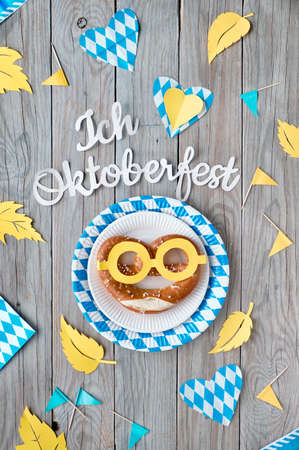 Paper text "I love Oktoberfest", flat lay on rustic wooden table with funny pretzel in paper glasses on paper plate, decorative hearts, flags and Autumn leaves.の写真素材