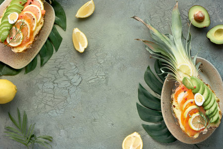 Top view on pinapple boats with smoked salmon and avocado slices with lemon and quail eggs, flat lay...