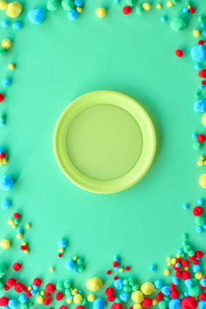 Empty disposable plastic plate on light green paper background with frame made of ittle fluffy balls, copy-spaceの写真素材