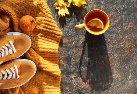 Autumn flat lay with yellow sweater, sneakers, decorative pumpkins, oak leaves and cup of tea with...