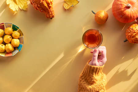 Yellow paper flat lay with copy-space. Female hand with cup of tea, orange pumpkins and paper plate with quince.の写真素材