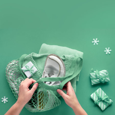 Packing presents, blue sweater in string bag, or mesh bag. Wintertime composition, flat lay on green...