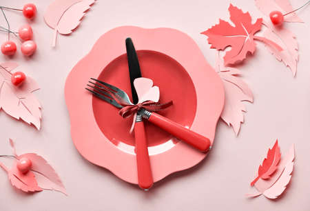 Table setup for Autumn celebration, coral color toned image. Thanksgiving or birthday. Bright plastic plate with fork and knife on yellow paper with paper Autumn leaves and berriesの写真素材