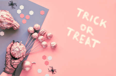 Creative paper craft Halloween flat lay on pink and grey split paper background with eyes and spiders. Hands in black mesh gloves holding decorations. Text "Trick or treat".の写真素材