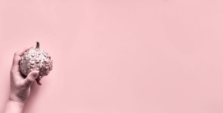 Halloween panoramic image toned in pink with hand holding decorative pumpkin painted metallic pink...