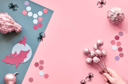 Creative paper craft Halloween flat lay on pink and grey split paper background with copy-space. Hand holding pink painted pumpkin,  bats, black spiders and hexagons.の写真素材