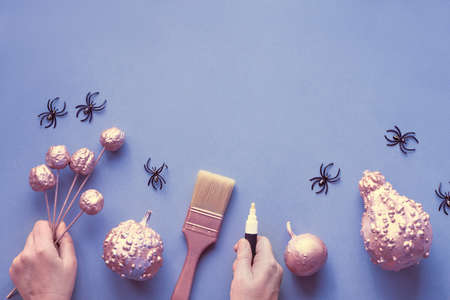 Creative Halloween flat lay on grey paper on light purple background with copy-space. Female hands holding marker and decorative pumpkins, plastic spiders and paint brush.の写真素材