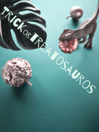 Dinosaur and halloween pumpkins on in biscay green background with exotic leaf with text "trickortreatosaurus", imaginary species of Halloween dinosの写真素材