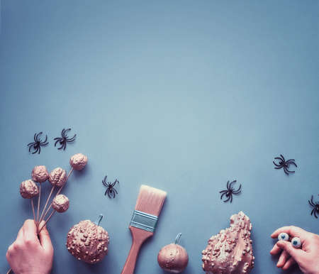 Creative Halloween flat lay on blue-grey paper background with copy-space. Frame made of decorative painted pumpkins, hands in black gloves imitating spiders with chocolate eyes.の写真素材