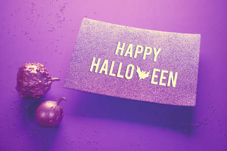 Creative pink and purple Halloween background on neon paper with glittering pumpkin painted metallic. Spotlight shining from underneath glittering paper card with text "Happy Halloween".の写真素材