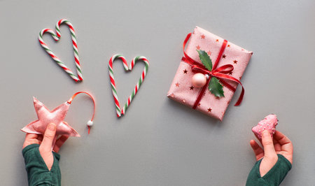 Festive Christmas background with wrapped pink gift box with bauble and holly leaf, hearts made of...