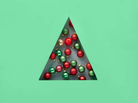 Geometric creative Christmas flat lay in neo mint and red colors with Xmas baubles in triangular paper hole in a shape of Christmas tree.の写真素材