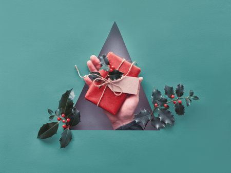Toned turquoise paper Xmas background with triangular hole in the middle. Hand holding wrapped...