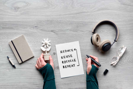 Concept zero waste conscious consumption flat lay, Top view of hands holding wooden flower, notebook with cover from craft cardboard, reading glasses and earphones on wooden table. Minimal lifestyle.の写真素材
