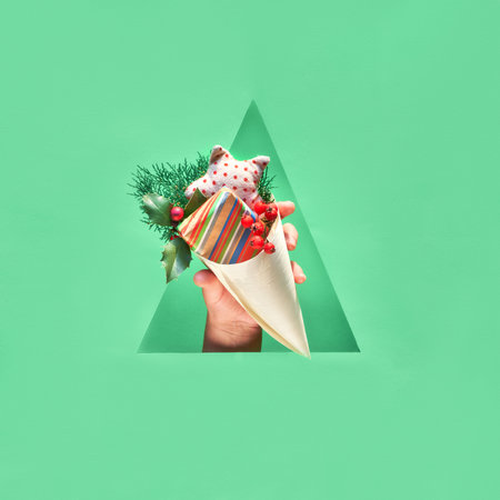 Hand with natural decorations and eco friendly gift in plywood cone showing out of triangular paper...