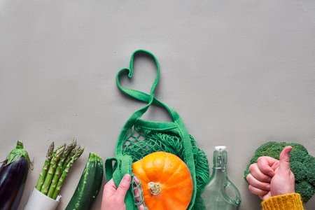 Eco friendly zero waste flat lay with hands holding broccoli and string bag with orange pumpkin....