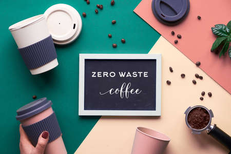 Zero waste coffee concept. Eco friendly reusable coffee cups in hands, geometric flat lay on split paper, creative background in green, beige and yellow with white chalk text on black board.の写真素材