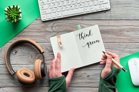 Think green, zero waste creative flat lay. Top view with hands holding notebook with motivation text, wooden workspace with keyboard, computer mouse, succulent plant, earphones on wooden table.の写真素材