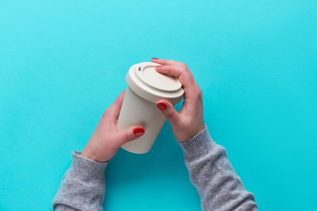 Hands holding reusable coffee cup made from eco friendly bamboo with silicone lid without plastic....