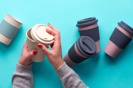 Assorted bamboo travel reusable coffee or tea cups or mags with silicone insulation.Hands open silicon lid on white mug. Eco friendly zero waste solution for low impact sustainable lifestyle.の写真素材