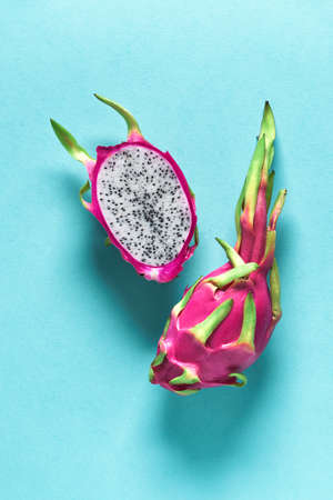 Fresh organic dragonfruit (pitaya or pitahaya) cut in half on blue mint background with shadows. Creative flat layout with trendy exotic fruit in vibrant bold pink and green colors.の写真素材