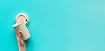 Stylish reusable eco coffee travel mug, bamboo cup with lid in hands. Blue mint paper background, panoramic image with copy-space. Minimalist zero waste eco friendly lifestyle trend.の写真素材